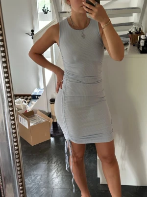 Ljusblå ribbad kort klänning M - Säljer en ljusblå ribbad kort klänning med snörning i sidorna. Klänningen är ärmlös och har en kroppsnära passform som framhäver figuren. Perfekt för dig som gillar en enkel men snygg stil.