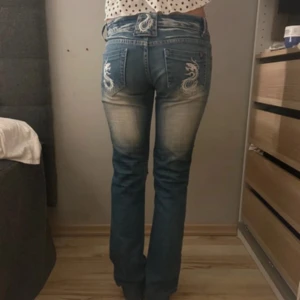 Blå jeans med drakbrodyr - Blå jeans med snygga broderade detaljer fram och bak. Smickrande passform med låg/normal midja och lätt utsvängda ben. Mjuk och bekväm denim, perfekta till både vardag och fest. Fint skick ✨ Midjemått:36cm och innerbenslångd:80cm så typ strl M  