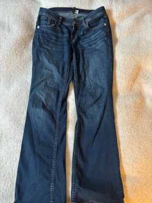 Mörkblå bootcut jeans  - Säljer ett par lågmidjade mörkblå bootcut jeans med snygga kontrastsömmar på bakfickan. Jeansen är från H&M och är i storlek 40🤍