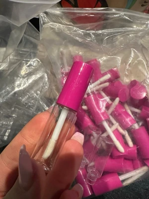 Tomma läppglansflaskor med rosa lock - Säljer tomma läppglansflaskor i genomskinligt plast med pensel och skruvlock i stark rosa plast. Perfekt för att blanda egna läppglans eller förvaring av nagelvårdsprodukter. Smidig och klassisk cylinderformad design. Tyvärr finns inga stoppers därav priset. Cirka 60 stycken