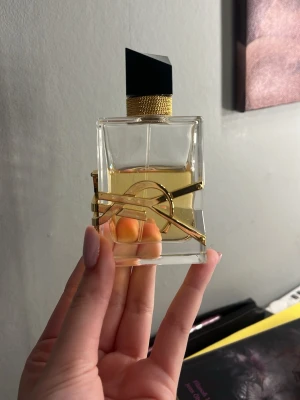 Yves Saint Laurent Libre parfym - Säljer en elegant parfym från Yves Saint Laurent, Libre. Flaskan är rektangulär i genomskinligt glas med guldiga detaljer och en stor svart asymmetrisk kork. Den har en lyxig känsla och den ikoniska YSL-loggan i guld runt flaskan. Mer än halva kvar!