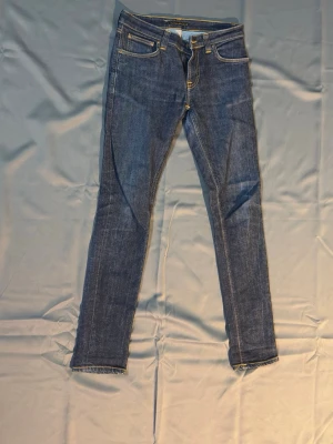 Blå jeans från Nudie Jeans Co - Snygga blå jeans från Nudie Jeans Co med klassisk femficksdesign och kontrastsömmar. Jeansen har smal passform och är tillverkade i slitstarkt denimtyg. Perfekta för en trendig och avslappnad look.