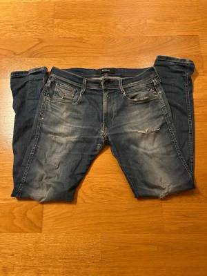 Replay anbass - Säljer ett par blå anbass jeans från Replay med slitningar och tvättade detaljer. Jeansen har fem fickor, slim passform. Slitningar vid knänen och vid låret. Lite sytt i mitten men syns inte när de används för att det är nästan under. Hålet där bak märks inte av när de används för att det är underifrån när de används. Storleken är 32/32. Tveka inte vid frågor. Kan skicka fler bilder vid fråga.