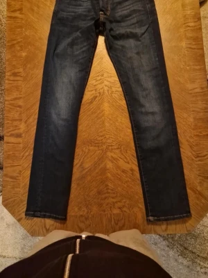 Mörkblå slim fit jeans - Snygga mörkblå slim fit jeans med klassisk femficksdesign och kontrastsömmar. Jeansen har raka ben och är tillverkade i ett stretchigt denimtyg som ger en bekväm passform. Perfekta för en stilren och avslappnad look.