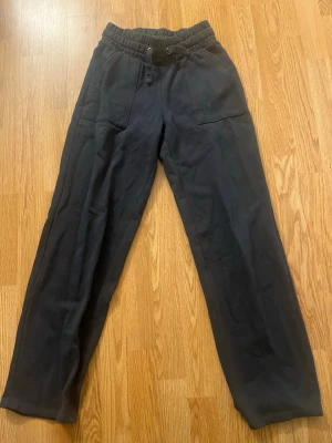 Svarta mjukisbyxor med resårmidja - Säljer ett par svarta mjukisbyxor med resår i midjan och dragsko. Byxorna har raka ben, två stora fickor fram och två bakfickor. Perfekta för chill dagar eller när du vill vara bekväm. Materialet känns mjukt och skönt mot huden.