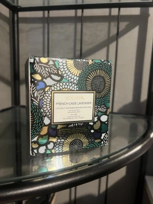 Voluspa French Cade Lavender ljus - Säljer ett Voluspa French Cade Lavender doftljus i ett ljusblått glas med dekorativt mönster. Kommer i en snygg förpackning med blommigt och färgglatt tryck. Ljusets doft är en mix av lavendel och trä, och vaxet är en kokosvaxblandning. Nypris 550