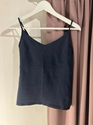 Mörkblå linnetopp med smala band - En stilren mörkblå linnetopp med smala axelband och v-ringad hals. Toppen är enkel och passar perfekt till jeans eller kjol. Tillverkad i mjuk bomull som känns skön mot huden. Perfekt för varma dagar eller som lager under en skjorta.