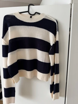 Randig stickad tröja från Divided - Säljer en snygg stickad tröja från Divided med breda marinblå och vita ränder. Tröjan har rund halsringning, långa ärmar och ribbade muddar. Perfekt för dig som gillar en avslappnad och trendig stil.