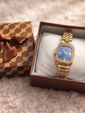 Guldfärgad klocka med blå urtavla - Snygg guldfärgad klocka från Winner med rektangulär blå urtavla och gnistrande stenar runt boetten. Länken är i metall och har en klassisk design som ger en lyxig känsla. Romerska siffror på urtavlan och detaljer i guld för extra stil.