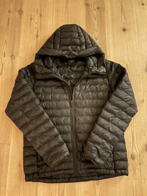 Everest jacka - Säljer en svart pufferjacka med huva och dragkedja framtill. Jackan har quiltad design och två sidofickor. Perfekt för kalla dagar och riktigt skön att bära. Materialet är lätt och isolerande, vilket gör den smidig att ha på sig under vintern.