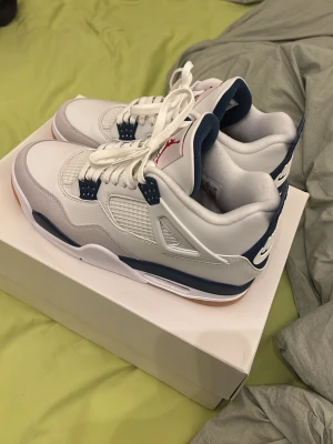 Nike SB Air Jordan 4 vit/marinblå - Nike SB Air Jordan 4 sneakers i vitt och marinblått med meshpaneler, klassisk Jumpman-logga på plösen och Nike SB-detalj på hälen. Skorna har en robust sula med gummidetaljer och coola plastdetaljer vid snörningen. Perfekt för dig som gillar streetwear och snygg design. ””jag har målat om sulorna själv eftersom det fanns färg fläckar från förut så den ser lite konstig ut där annars är det helt nytt””