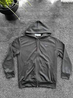 CDG Hoodie - Svart hoodie med dragkedja från Comme des Garçons Play. Har huva med dragsko, två fickor fram och ikoniskt hjärta med ögon på bröstet samt stort hjärta med ögon på ryggen. Storlek XXL men passar L, skick 10/10 som ny. Pris går att diskutera✅