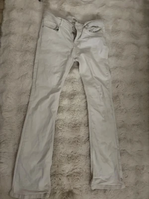 Vita bootcut jeans  - Säljer ett par vita jeans med bootcut passform och klassisk femficksdesign. Jeansen har normal/low midja och är tillverkade i ett mjukt bomullsmaterial. Perfekta för en clean och stilren look.