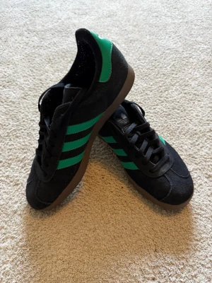 Adidas Gazelle svart/gröna - Säljer mina Adidas Gazelle svarta med gröna detaljer. För små för mig och har bara testa dem enstaka gånger, så de är i nytt skick. Köpta för 1350kr. Hör av dig för snabb affär eller frågor!