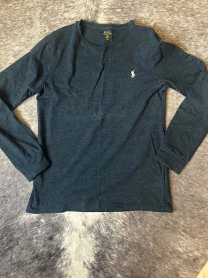 Mörkblå långärmad topp från Polo Ralph Lauren - Mörkblå långärmad topp från Polo Ralph Lauren med klassisk rund halsringning och broderad logga på bröstet. Tillverkad i mjuk bomull som känns skön mot huden. Perfekt för en avslappnad och stilren look.