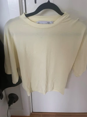 Ljusgul t-shirt från 157 - En basic ljusgul t-shirt från 157 i storlek XS. T-shirten har en klassisk rund halsringning och korta ärmar som markerar midjan. Perfekt för en enkel och fräsch stil, lätt att matcha med jeans eller shorts.