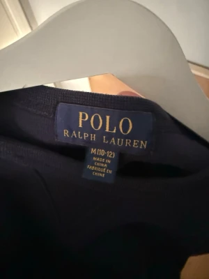 Mörkblå sweatshirt från Polo Ralph Lauren - Klassisk mörkblå sweatshirt från Polo Ralph Lauren med rund halsringning och diskret broderad logga på bröstet. Tröjan har långa ärmar och ribbade muddar vid ärmslut och nederkant. Perfekt för en stilren och avslappnad look.