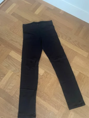 Svarta höga leggings - Säljer ett par svarta leggings med hög midja och smal passform. De är stretchiga och sitter tight längs benen, perfekta till oversized tröjor eller hoodies. Materialet känns mjukt och bekvämt, troligen bomullsmix eller liknande. Inga synliga detaljer eller loggor.