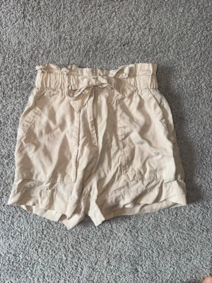 Beiga highwaist shorts med knytband - Snygga beiga shorts med  knytband i midjan. De har två fickor framtill och en lös, avslappnad passform. 