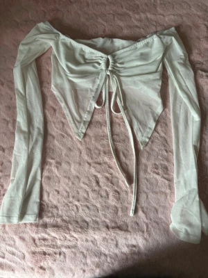 Vit offshoulder topp med snörning - Trendig vit offshoulder topp med långa ärmar och snörning framtill som ger en snygg draperad effekt. Toppen har en croppad passform och spetsig nederkant framtill. Perfekt för dig som vill sticka ut med en unik och stilren look.