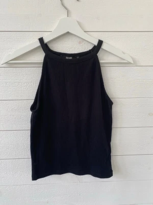 Svart ribbad linnetopp från Bik Bok - Snygg svart ribbad linnetopp från Bik Bok med hög hals och ärmlös design. Perfekt att matcha med jeans eller kjol för en stilren look. Mjuk och stretchig i materialet för extra komfort.