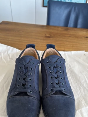 Christian Louboutin - Snygga mörkblå sneakers från Christian Louboutin i mocka med klassisk röd sula och diskret logga undertill. Skorna har rund tå, platta skosnören och låg profil. Perfekta för dig som vill sticka ut med exklusiv stil.