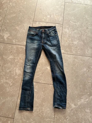 Blå slim fit jeans med slitningar - Snygga blå slim fit jeans med slitningar och tvättade detaljer. Klassisk femficksmodell med dragkedja och knapp i midjan. Jeansen har en modern passform och coola slitningar på både fram- och baksida. Perfekta för en trendig och avslappnad stil.