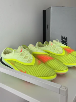 NIKE PHANTOM 6 Elite  - Säljer ett par Nike Mercurial Vapor 15 fotbollsskor i neon-gult med svarta och rosa detaljer. Skorna har en strömlinjeformad design, snörning och ovandel i syntetmaterial för bra bollkontroll. Perfekta för dig som vill sticka ut på planen.