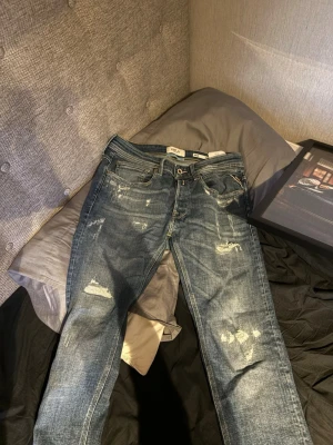 Blå slitna jeans från replay - Säljer ett par blå jeans från Nudie Jeans med snygga slitningar och distressed detaljer. Klassisk femficksmodell med normal passform och läderpatch bak i midjan. Perfekta för en avslappnad och trendig look. Nypris 2000 mitt pris 600 