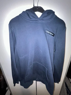 Mörkblå hoodie från Peak Performance - Snygg mörkblå hoodie från Peak Performance med klassisk huva och magficka. Diskret logga på bröstet och mjukt material som känns skönt mot huden. Perfekt för dig som gillar enkel och stilren design. Finns lite färg men för det emdta bara på insidan(bilden)