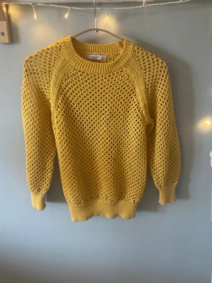 Gul stickad tröja från Mango - Snygg gul stickad tröja från Mango Basics med grovmaskigt mönster och rund halsringning. Tröjan har långa ärmar och ribbade muddar vid ärmslut och nederkant. Perfekt för att liva upp din outfit med en pop av färg.