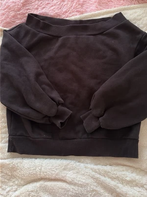 Svart  off shoulder hoodie utan tryck - En svart hoodie i enkel och stilren design, utan tryck eller logga. Tröjan har långa ärmar, breda muddar vid ärmslut och nederkant samt en klassisk passform. Perfekt för en avslappnad look. Materialet är mjukt och bekvämt, troligtvis bomullsblandning.