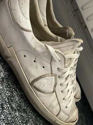 Vita Philippe Model sneakers - Snygga vita sneakers från Philippe Model med klassisk låg siluett. Skorna har läderöverdel, vita skosnören och ikonisk sköldlogga på sidan. Yttersulan är i gummi och märkt med Philippe Model Paris. Perfekta för en clean och stilren look.