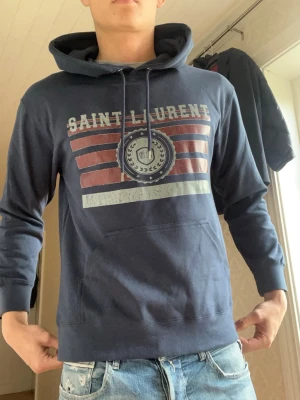 Blå Saint Laurent hoodie - Snygg blå hoodie från Saint Laurent med lapp kvar såklart. Pris kan diskuteras vid snabb affär!