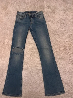 Blå slitna jeans från Jack & Jones - Säljer ett par blå jeans från crocker med rak passform och slitning på vänster knä. Jeansen har klassisk femficksdesign, bälteshällor och dragkedjegylf. Materialet är denim i bomull med en skön tvättad look.