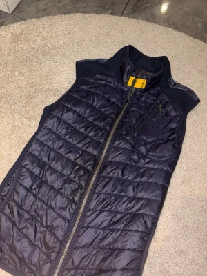Mörkblå dunväst från Parajumpers‼️Går också att byta mot skor eller kläder‼️ - Snygg mörkblå dunväst från Parajumpers med gul detalj vid kragen och orange insida. Västen har dragkedja framtill, bröstficka med dragkedja och quiltad design. Perfekt för lager på lager och streetwear-stil. 