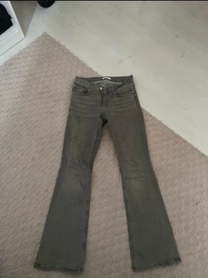 Grå bootcut jeans med låg midja - Snygga grå bootcut jeans med låg midja och klassisk femficksdesign. Jeansen har en lätt utsvängd passform nertill och stängs med dragkedja och knapp. Perfekta för en avslappnad och trendig look.