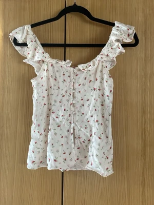 Vit blommig blus med volang - Söt vit blus med små blommor i rött och grönt. 
