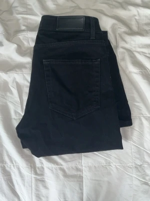 Svarta skinny jeans med fem fickor - Snygga svarta skinny jeans med klassisk femficksdesign och svarta sömmar. Jeansen har en stilren look med bälteshällor och knappstängning. Perfekta för dig som gillar en slimmad passform och enkel stil.