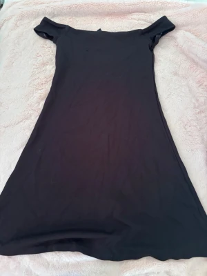 Svart offshoulder kortklänning från Italien  - En svart, enkel och stilren kortklänning med offshoulder-design. Köpt på hm i Italien Klänningen har en rak passform och är tillverkad i ett mjukt material som ger en bekväm känsla. Perfekt för dig som gillar minimalistisk stil och vill ha något lättmatchat.