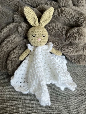 Virkad snuttefilt kanin - Supergullig handvirkad snuttefilt i form av en kanin med beige huvud och öron samt vit filt. Kaninen har broderade ögon och nos, och filten är mjuk och fluffig. Perfekt som mysig kompis till små barn eller som present.