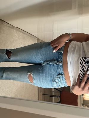 Ljusblå raka jeans med hål - Säljer ett par ljusblå jeans med raka ben och slitna hål på båda knäna. Jeansen är mid wasted och finns ej kvar på Ginas hemsida. Haft på mig 2-3 gånger 