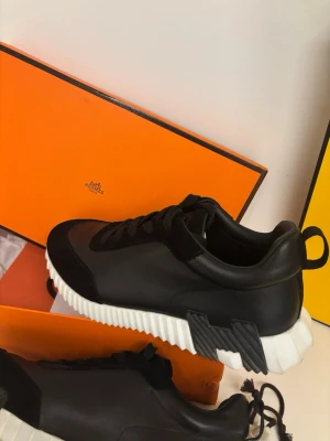 Svarta H sneakers - Snygga svarta sneakers från H med chunky vit sula och svarta detaljer på sidan. Skorna har en låg silhuett, rund tå och är tillverkade i läder med textildetaljer. Perfekta för dig som gillar exklusiv och modern streetstyle.