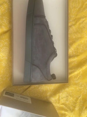 Grå sneakers från Christian Louboutin - Snygga grå sneakers från Louboutin i mocka med matchande grå snörning och gummisula. Skorna har en stilren design och är perfekta för dig som gillar en clean look. Insidan är fodrad i läder för extra komfort.