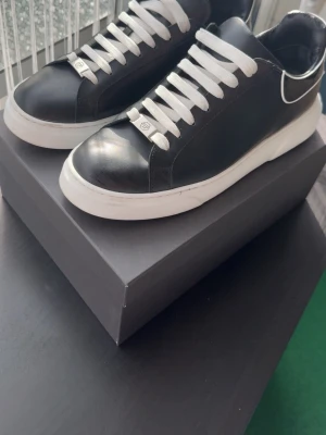 Philipp Plein svarta sneakers med vit sula - Svarta sneakers från Philipp Plein med vit tjock sula och vita skosnören. Skorna har en stilren design i läder och detaljer med logotyp och dödskalle på hälen. Perfekta för dig som gillar streetstyle och exklusiva märken.