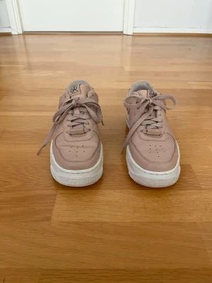 Nike Air Force 1 Pixel – storlek 37.5 - Säljer ett par Nike Air Force 1 Pixel i ljus rosa/beige färg, storlek 37.5. Skorna är använda men fortfarande i bra skick och väldigt bekväma. De har en stilren och trendig design som passar både till vardag och mer uppklädda outfits. Däremot förekommer ett fåtal små defekter inuti skon se på bild för egen bedömning.