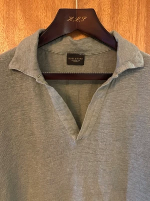 Rose & Born polo - Snygg grå polo från Rose & Born med öppen krage och korta ärmar. Toppen har en avslappnad passform och är tillverkad i ett luftigt linnematerial, perfekt för varma dagar. Enkel men stilren design som funkar till mycket.