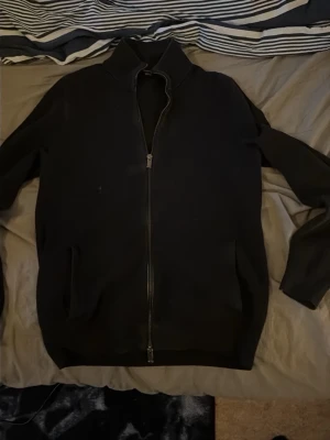 Svart ziptröja från Massimo Dutti - Stilren svart ziptröja från Massimo Dutti i exklusiv bomull. Tröjan har hög krage, hel dragkedja framtill och två fickor. Perfekt för en clean och avslappnad look. Ny pris 900kr.
