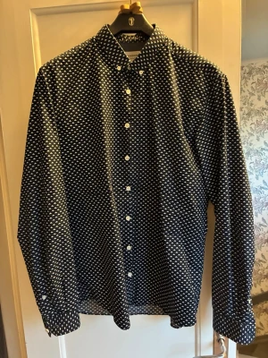 Mönstrad skjorta från Lindbergh - Snygg svart skjorta från Lindbergh med vitt geometriskt mönster. Skjortan har klassisk krage, knäppning framtill och långa ärmar. Perfekt för dig som vill sticka ut lite extra med din stil.