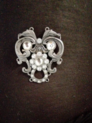 Vintageinspirerad brosch i silverfärg - Snygg brosch i antiksilver med glittrande klara stenar och dekorativa snirkliga detaljer. Perfekt som statement-accessoar till jacka eller väska. Materialet är metall med infattade glasstenar i olika storlekar och former.